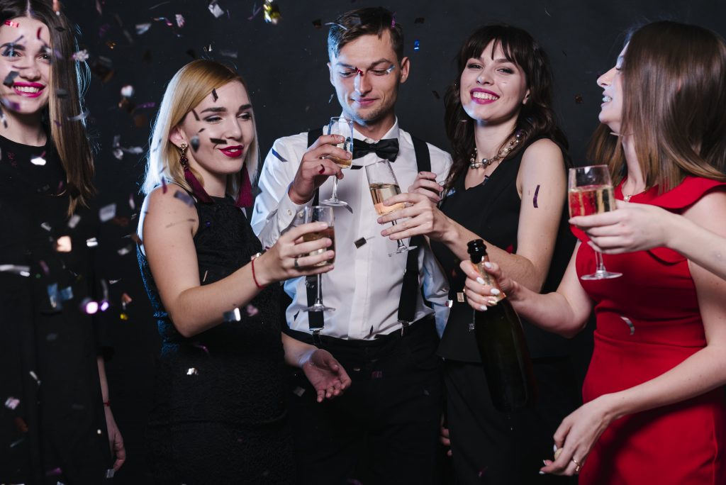 smiling-ladies-guy-evening-wear-with-glasses-drinks-tossing-confetti-min